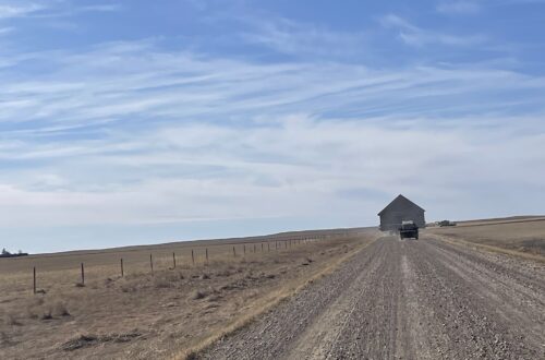 Gravel road under expansive blue sky to barn